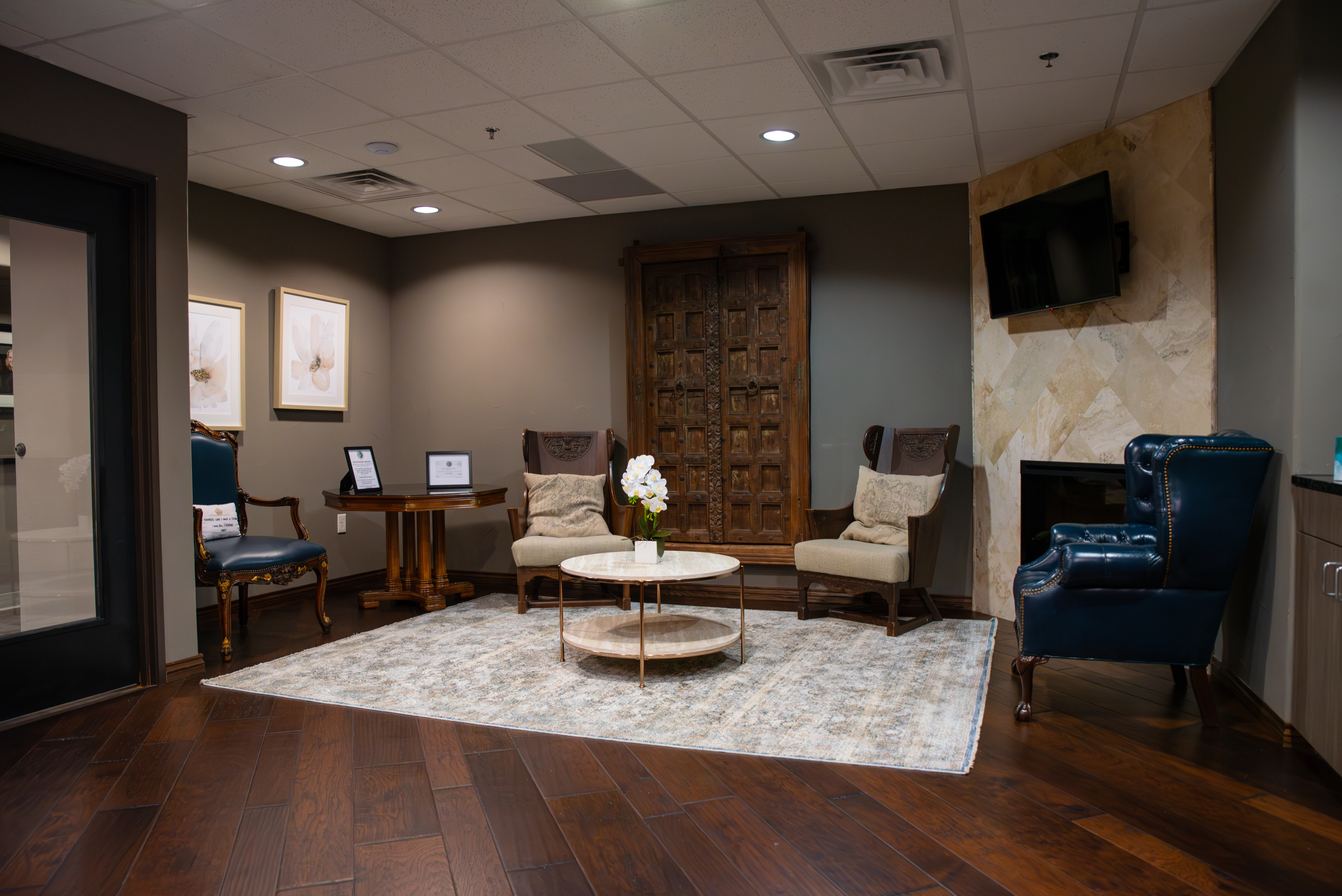 Luminescence Dentistry Waiting room with three elegant wooden chairs, a dark blue couch and a small beige center table